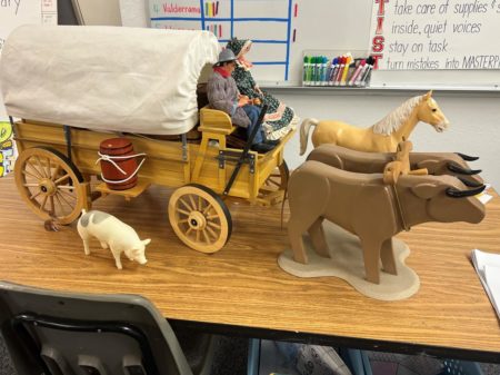 This photo shows a prop used in a lesson on the Santa Fe Trail. It includes a toy wagon with two passengers pulled by oxen and accompanied by a horse and a pig.