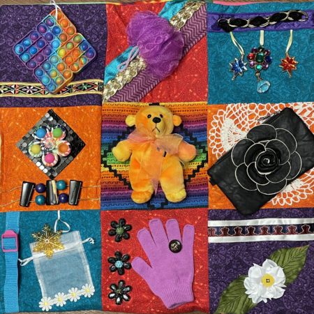 This photo is a close up of a fidget quilt showing nine squares of the quilt, with a small teddy bear in the middle.
